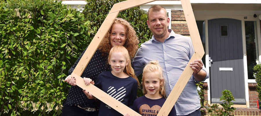 Een gezin met een houten frame voor een huis.