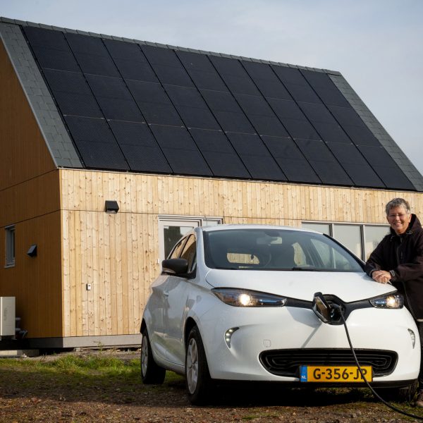 Een vrouw staat naast een elektrische auto voor een huis met zonnepanelen.