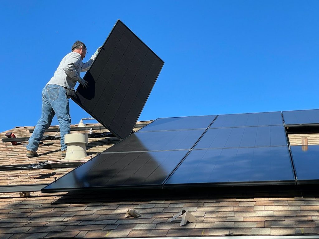 Een man die zonnepanelen op een dak installeert.