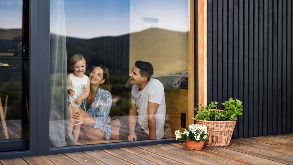 Een gezin zit op een houten terras achter het glas met een kindje in hun armen.