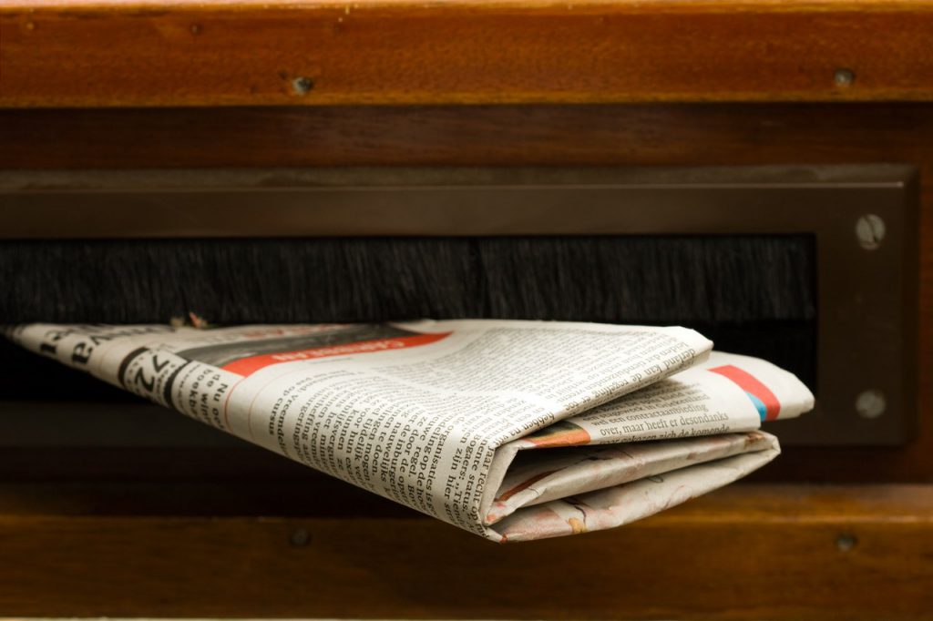 Een krant zit in een houten brievenbus.