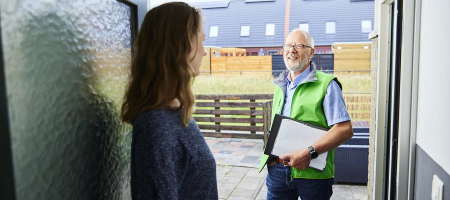 Een man in een groen vest praat met een vrouw in een deuropening.
