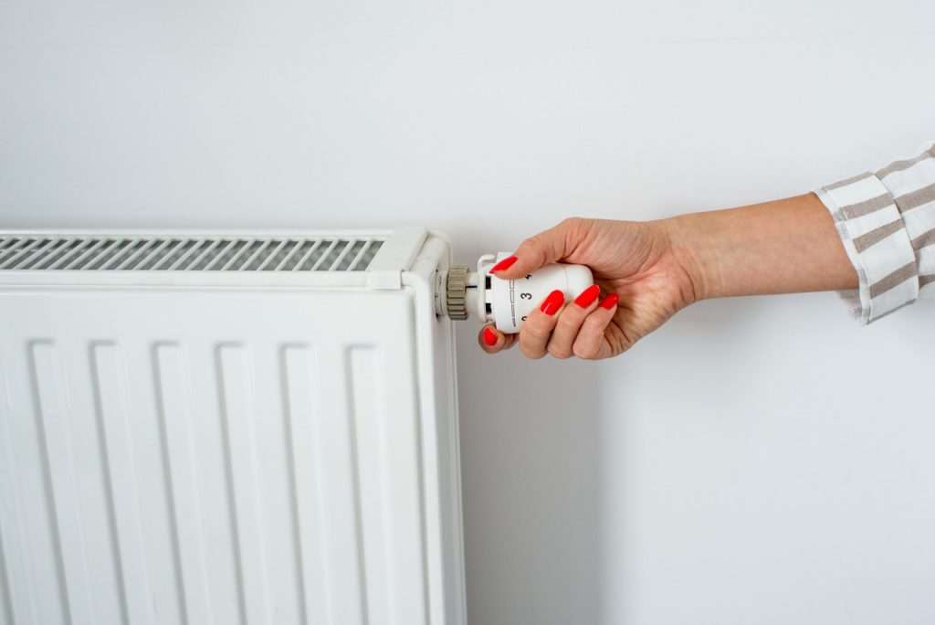 De hand van een vrouw houdt een witte radiatorknop vast.