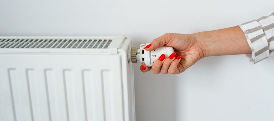 De hand van een vrouw houdt een witte radiatorknop vast.
